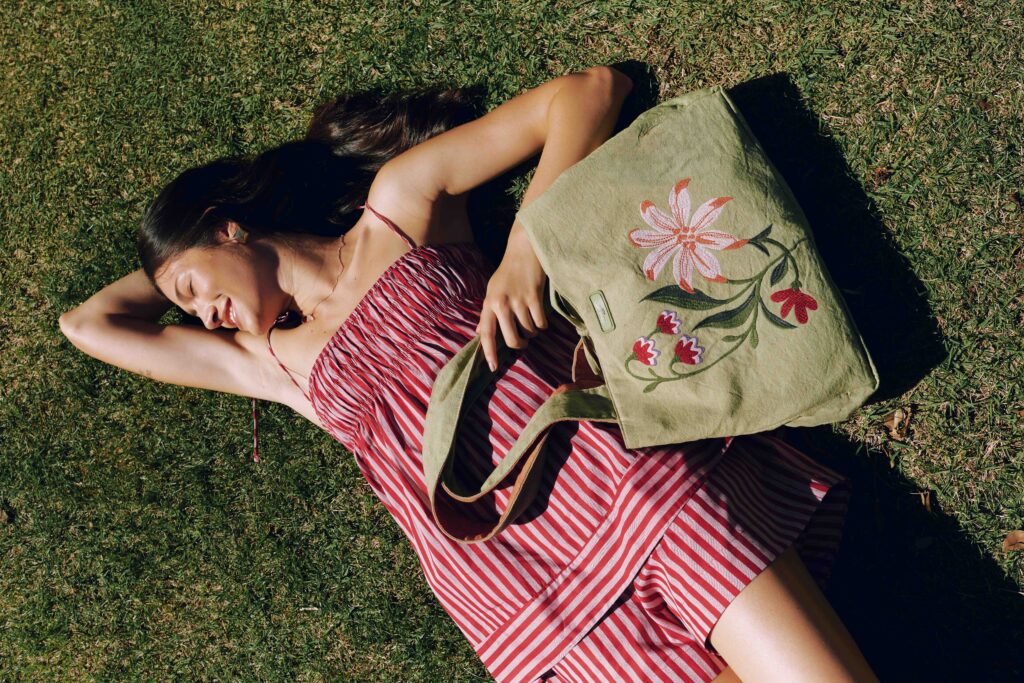 Mulher com cabelos longos usando vestido vermelho e uma bolsa verde estampada 