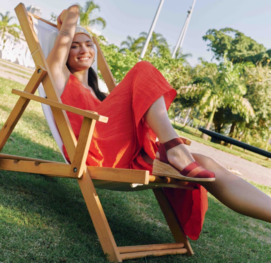 Mulher com vestido vermelho sorrindo e mostrando sua sandália