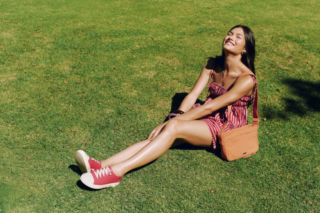 Mulher com cabelos longos e pretos, de vestido vermelho e sapatos vermelhos, usando uma bolsa laranja.