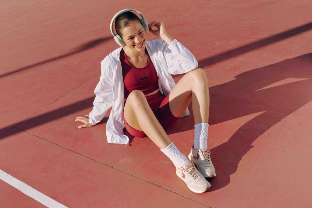 Mulher com roupa de academia vermelha e blusa branca sentada em uma pista de corrida 