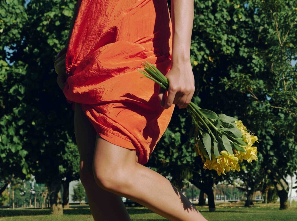 Mulher de vestido laranja segurando flore amarelas